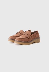 Mocassins en suede marron avec un bout arrondi, ornés de coutures décoratives, d'une semelle plateforme et d'un détail de logo subtil sur le côté.