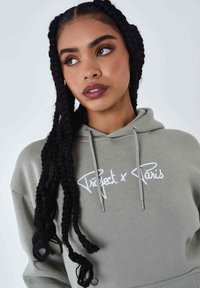 Olijfgroene hoodie met witte geborduurde tekst "Project x Paris," voorzien van een trekkoordcapuchon en contrasterende zilveren accenten.