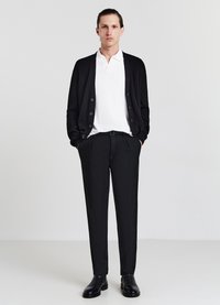 Cardigan nero su un polo bianco a coste, abbinato a pantaloni neri su misura e stivaletti. Presenta una chiusura frontale con bottoni e un design slim fit.