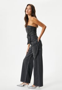 Top negro sin mangas con cintura cinturilla, combinado con jeans de mezclilla negros holgados y zapatos plateados de punta. Diseño simple y texturizado.