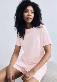 Ροζ βαμβακερό T-shirt με κοντά μανίκια, με διακριτικές λεπτομέρειες στους ώμους και μικρό λευκό λογότυπο. Συνδυάζεται με αντίστοιχα σορτς.