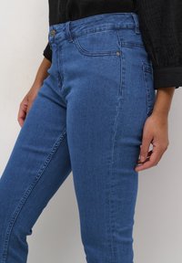 Siniset farkut korkealla vyötäröllä, slim fit -mallilla ja lievällä joustavuudella. Ominaisuuksiin kuuluu etutaskut, metalliosat ja sileä pinta.