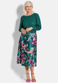 Pull en tricot vert à manches longues, associé à une jupe à imprimé floral comportant des fleurs roses et vertes, et des sandales roses à lanières.