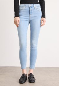Jean skinny bleu clair en denim, avec taille haute, légère décoloration, design à cinq poches et fermeture à bouton. Associé à des mocassins noirs.