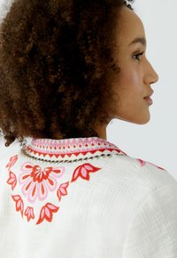 Witte geborduurde kleding met kleurrijke bloempatronen in roze en rood. Textuurstof met decoratieve kraagdetails.