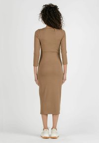 Figurschmeichelndes, langärmeliges Midikleid aus hellbraunem Material mit glatter Textur und einem subtilen Nahtdetail in der Taille.