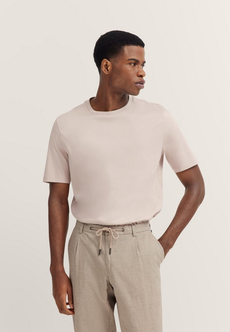 Short-sleeve, crew-neck shirt in light pink, made of smooth fabric, paired with beige trousers featuring an elastic waistband and drawstring.