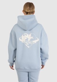Felpa oversize azzurro chiaro in cotone con una grafica bianca di un cuore che circonda dei globo e il testo "SMILODOX" sul retro.