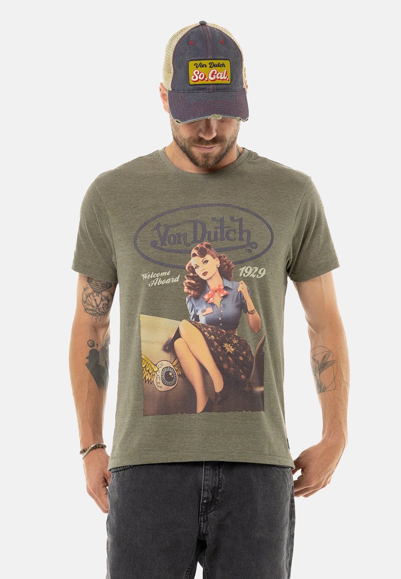 T-shirt en coton vert olive avec un imprimé de style vintage représentant une femme. Associé à une casquette ajustable multicolore arborant un logo bien visible.