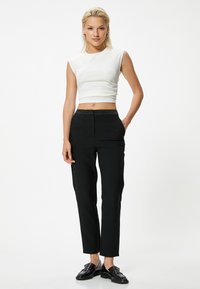 Witte mouwloze crop top met een lichte glans, gecombineerd met op maat gemaakte zwarte broek met een gladde afwerking en zijzakken. Zwarte instappers maken de look compleet.