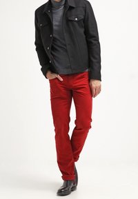 Giacca di jeans nera con colletto, t-shirt grigia e pantaloni rossi attillati. Gli stivali di pelle nera completano l'outfit.