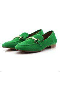 Mocasines de ante verde con punta afilada, que presentan un acento de metal dorado y un tacón de madera plano. Textura suave con costuras en contraste.
