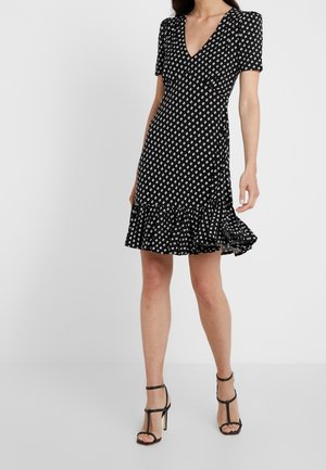 Czarna sukienka krótko rękawowa z białym nadrukiem liści, dekolt w serek, dopasowany w pasie i rozkloszowany dół. Założona z czarnymi sandałami na wysokim obcasie z paskami.