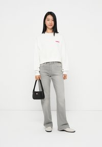 Witte cropped sweatshirt met een rood "TOMMY" logo, gecombineerd met lichtgrijze flared jeans. Zwarte handtas met een korte schouderband. Neutrale schoenen.