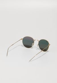 Occhiali da sole rotondi con montatura in metallo dorato, lenti verde scuro e tempie sottili. Include naselli trasparenti per comfort e stabilità.