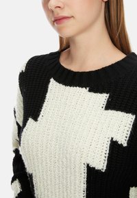 Schwarz-weißer gestrickter Pullover mit geometrischem Muster, rundem Ausschnitt und strukturiertem Stoff.