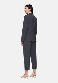 Gray tailored suit jacket and tapered trousers, made of smooth fabric, featuring a notch collar, button details, and rolled cuffs. White heeled shoes.