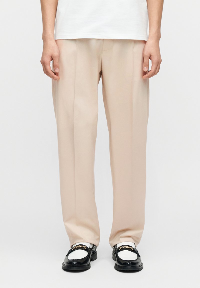 Φωτεινό μπεζ παντελόνι καλοραμμέν ο με άνετη εφαρμογή, με απαλή υφή, μονό πιέτα και ίσια γραμμή στο πόδι. Συνδυάζεται με μαύρα λοφάρια.