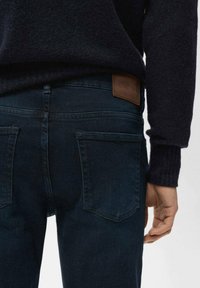 Jeans azul oscuro hechos de mezclilla, con un diseño clásico, dos bolsillos traseros y una parche de cuero marrón en la cintura.