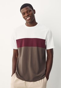 Heren t-shirt met korte mouwen, bestaande uit een wit bovenstuk, een bordeauxrode horizontale streep en een donkergrijze onderkant. Gemaakt van een zachte katoenmix.