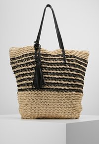 Tkaná slamá taška s černými a přírodními pruhy. Obsahuje dvě černé kožené uši a dekoraci v podobě třásně. Prostorný design.