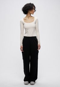 Fehér hosszú ujjú felső négyzet alakú nyakkivágással, fekete, széles szárú cargo nadrággal párosítva, oldalzsebekkel és laza szabással.