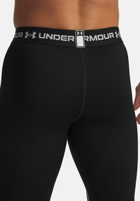 Black compression leggings with a textured fabric, featuring an elastic waistband with "UNDER ARMOUR" logo in white and grey accents.