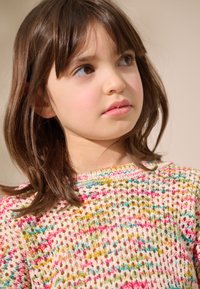 Pull en maille crème avec des taches multicolores de rose, vert et bleu. Il présente un col rond et une texture lâche et aérée.