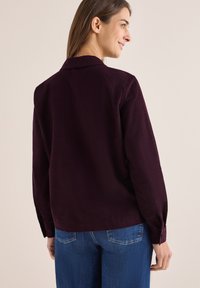 Mørk burgunder langærmet skjorte med krave, der har en afslappet pasform og knapmanchetter, parret med blå jeans.
