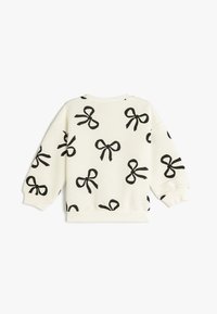 Sweatshirt blanc avec un design côtelé texturé, présentant des motifs de nœuds noirs. Poignets et ourlet élastiques. Encolure ronde, style décontracté.