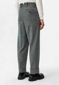 Grijze gestreepte broek met een hoge taille, taps toelopende benen en een omgeslagen zoom. Voorzien van één achterzak met knoopsluiting.