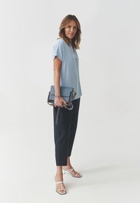 Blusa de manga corta azul claro con botones, combinada con pantalones de color navy. Un bolso azul con bandolera y tacones blancos con tiras.