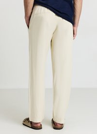 Pantaloni beige chiaro con vestibilità comoda e vita elastica, dotati di tasche laterali e realizzati in tessuto liscio e strutturato. Nessun motivo o dettaglio visibile.