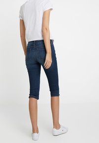 Tummansiniset farkku capri-housut slim fit -mallissa, joissa on käännetyt lahkeet ja huomaamattomat ompeluyksityiskohdat, yhdistettynä valkoiseen t-paitaan ja lenkkareihin.