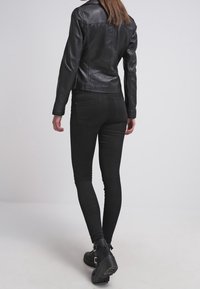 Black leather jacket with a fitted design, featuring a high collar and visible stitching, paired with black skinny jeans and ankle boots.