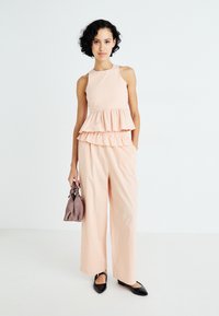 Top peplum de color durazno con capas con volantes, combinado con pantalones de pierna ancha. Presenta un diseño depurado y unos zapatos planos negros de punta.