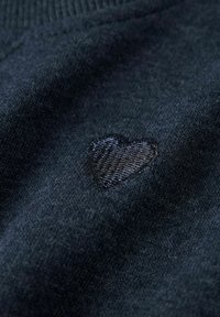 Tela de un oscuro azul marino con un pequeño corazón bordado en un azul ligeramente más claro. La textura es suave y está tejida con un acabado liso.