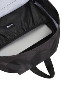Interior de mochila de tela negra con un forro gris, que presenta un compartimento para laptop y el logo de Vans. Exterior texturizado y asa para llevar.