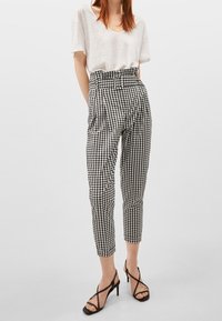 Schwarz-weiße Karo-Hosen mit hoher Taille und schmalem Bein. Kombiniert mit einem lockeren, hellgrauen kurzärmeligen Oberteil und Riemchenabsätzen.