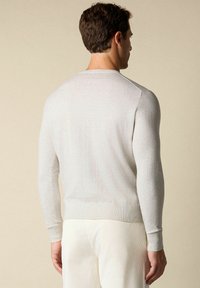 Světle šedý pletený svetr s dlouhými rukávy, žebrovanými manžetami a přiléhavým pasem. Měkká textura, minimalistický design, pohled zezadu.