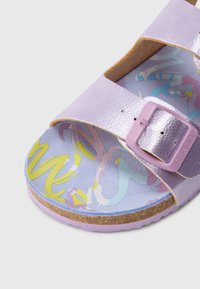 Μεταλλικό μωβ σανδάλι με δύο ρυθμιζόμενα λουριά και υφή σε αγκράφα. Η εσωτερική σόλα διαθέτει πολύχρωμο αφηρημένο μοτίβο σε ανοιχτό φόντο.