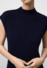 Top aderente navy a collo alto con maniche a cappuccio. Presenta una texture liscia e un raffinato dettaglio delle cuciture.
