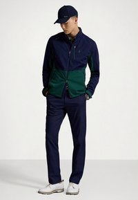 Tamsiai mėlyna ir žalia striukė su užtrauktuku ir aukštu apykakliu, derinama su tamsiai mėlynomis kelnėmis ir baltais bateliais. Komplekte yra juoda beisbolo kepurė.