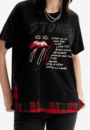 Camiseta de algodón negra con gráfico "STONES", diseño de labios rojos y texto blanco. Presenta un dobladillo de franela a cuadros en negro y rojo. Ajuste relajado.