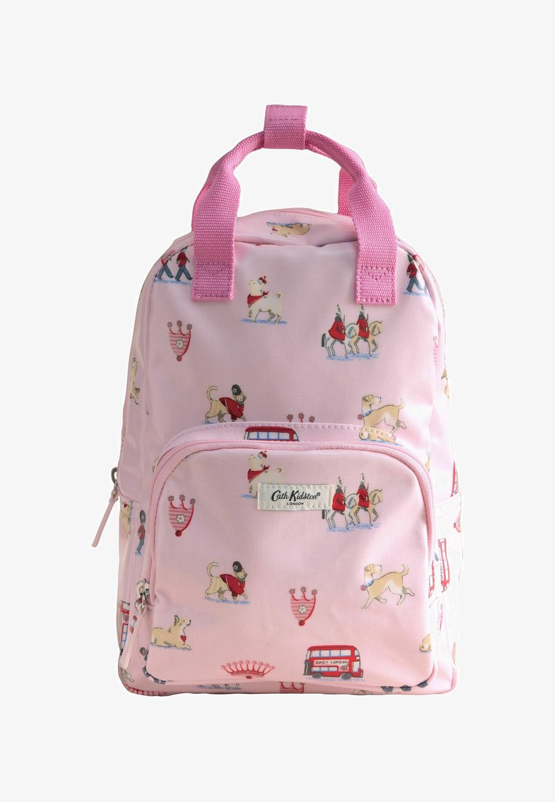 Sac à dos rose Cath Kidston avec des imprimés sur le thème de Londres, incluant des chiens, des gardes royaux, des bus à impériale et des couronnes, doté de poignées roses et d'une poche avant.