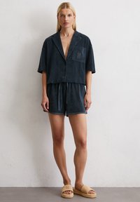 Dark blue, short-sleeve button-up shirt with a chest pocket, paired with matching shorts. Woven beige slide footwear completes the look.