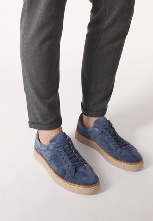 Modré semišové tenisky s perforovanou strukturou, bílou gumovou podrážkou a tkaničkami. Nosené s šedými tapered kalhotami, které mají ohrnuté manžety.