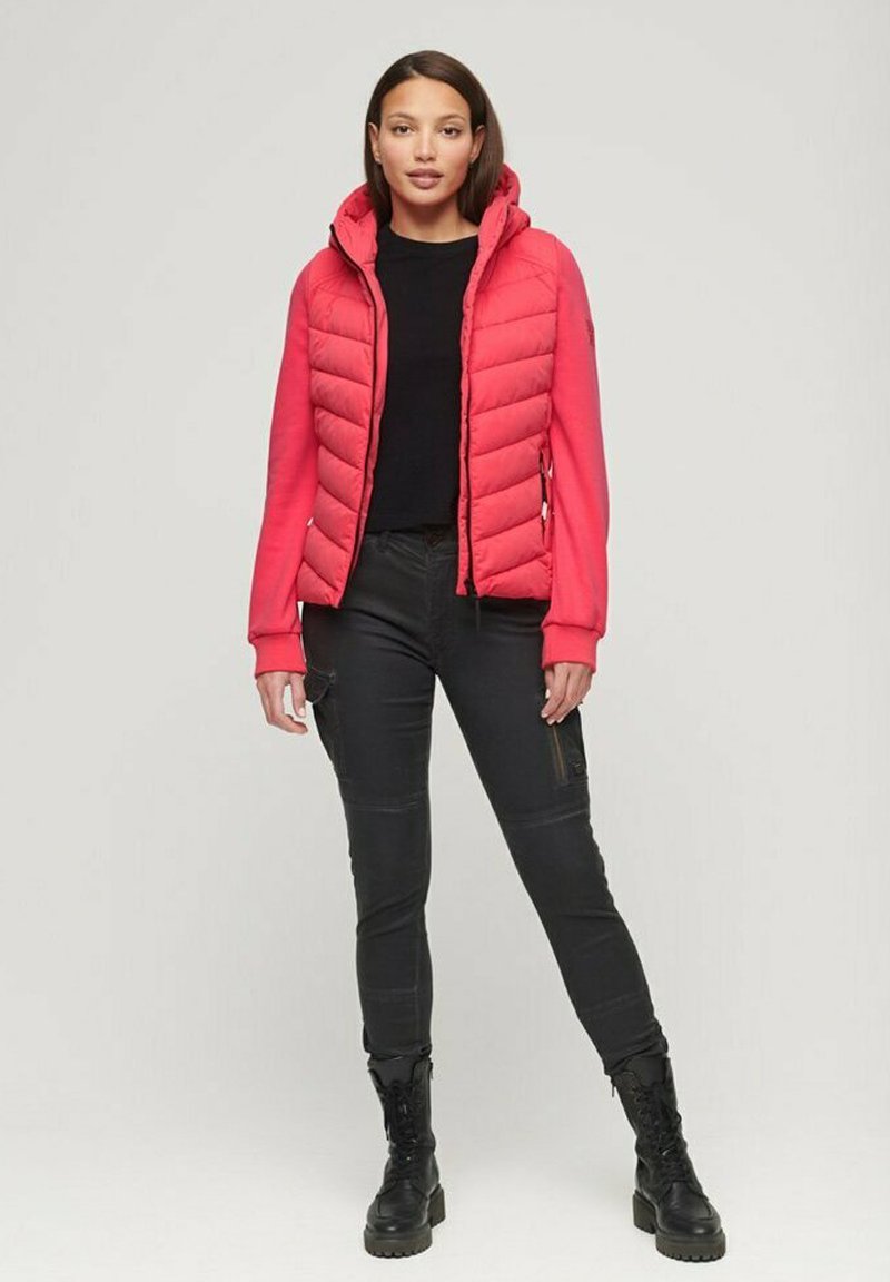 Rote Daunenjacke mit Kapuze, mit gestepptem Design und elastischen Bündchen, kombiniert mit schwarzen, enganliegenden Hosen und schwarzen Kampfboots.