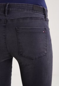 Vaqueros de mezclilla gris oscuro con un diseño ajustado, que cuentan con un único bolsillo trasero y una pequeña etiqueta de logo. Textura suave, con detalles mínimos.