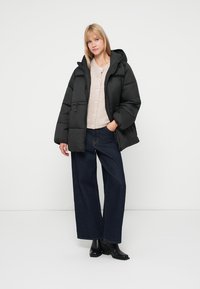 Black puffer jacket with a hood, featuring a zip closure and side pockets, layered over a beige knit cardigan and wide-leg blue jeans.